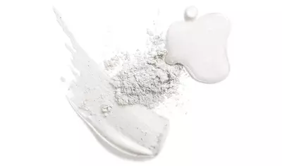 A collection of white cosmetic products, including a smooth cream, loose powder, and a swatch of textured cream, arranged artistically on a light background.