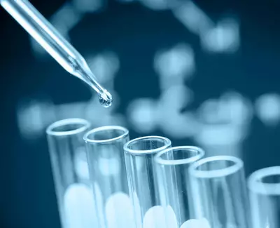 A dropper releasing a liquid droplet into a row of clear test tubes, with a blurred DNA structure in the background.