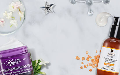 Produkter for hudvård från Kiehl's på en marmorbordsyta, inklusive flaskor och en kram.