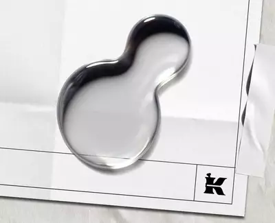 Två vattendroppar på ett tomt papper med en svart "K"-logga och en bit tejp hogst upp.