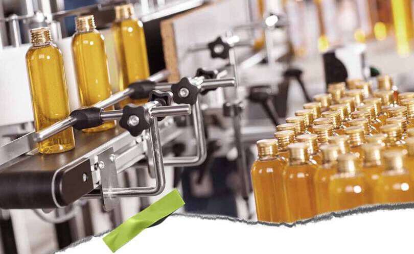 En automatiserad tappningslinje med genomskinliga flaskor fyllda med gul vatska och metallklammor, som visar en hektisk produktionsmiljo.