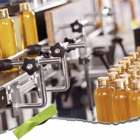 En automatiserad tappningslinje med genomskinliga flaskor fyllda med gul vatska och metallklammor, som visar en hektisk produktionsmiljo.