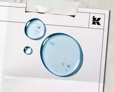 Två vattendroppar på ett tomt papper med en svart "K"-logga och en bit tejp hogst upp.