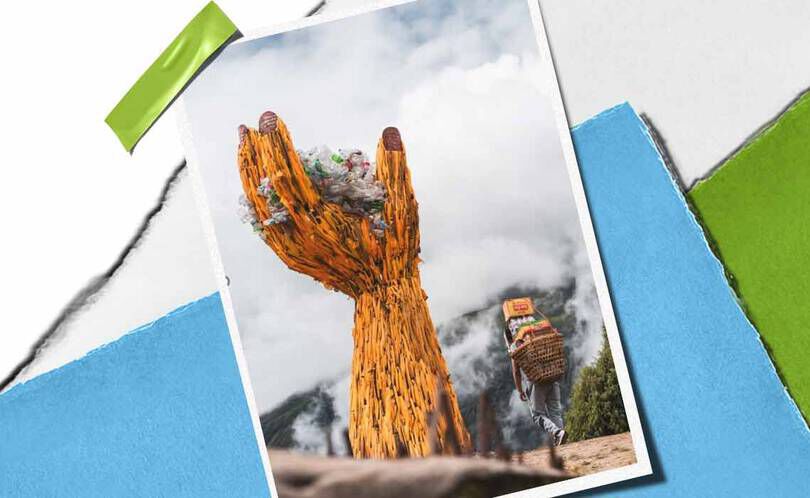 En hog handskulptur i tra håller en hog med skrap, som symboliserar miljomedvetenhet, med en person som bar varor i narheten.