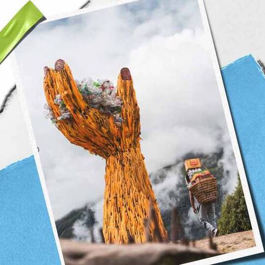 En hog handskulptur i tra håller en hog med skrap, som symboliserar miljomedvetenhet, med en person som bar varor i narheten.