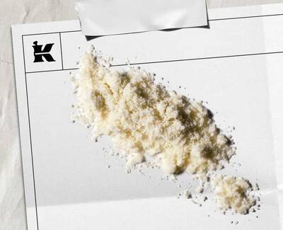 En hog med vitt pulver på ett tomt papper med en logotyp i hornet, vilket antyder en konstnarlig eller stilistisk presentation.