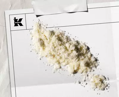 En hog med vitt pulver på ett tomt papper med en logotyp i hornet, vilket antyder en konstnarlig eller stilistisk presentation.