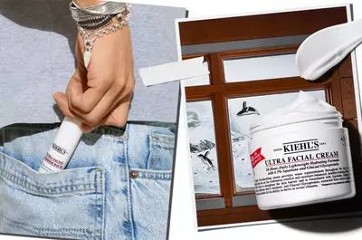 A person holds a tube of Kiehl's Ultra Facial Cream, partially visible from their back pocket, with a window showing a snowy landscape in the background.