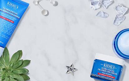 Produkter for hudvård från Kiehl's, inklusive ansiktskram, toner och gel, placerade på en marmorliknande yta med citronskivor och isbitar runtom.