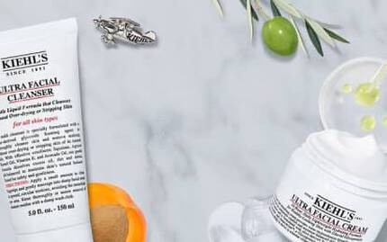 Produkter från Kiehl's for ansiktsvård, inklusive rengoringsgel, toner och ansiktskram, placerade på en marmor-bakgrund med citrusfrukt och olivblad.