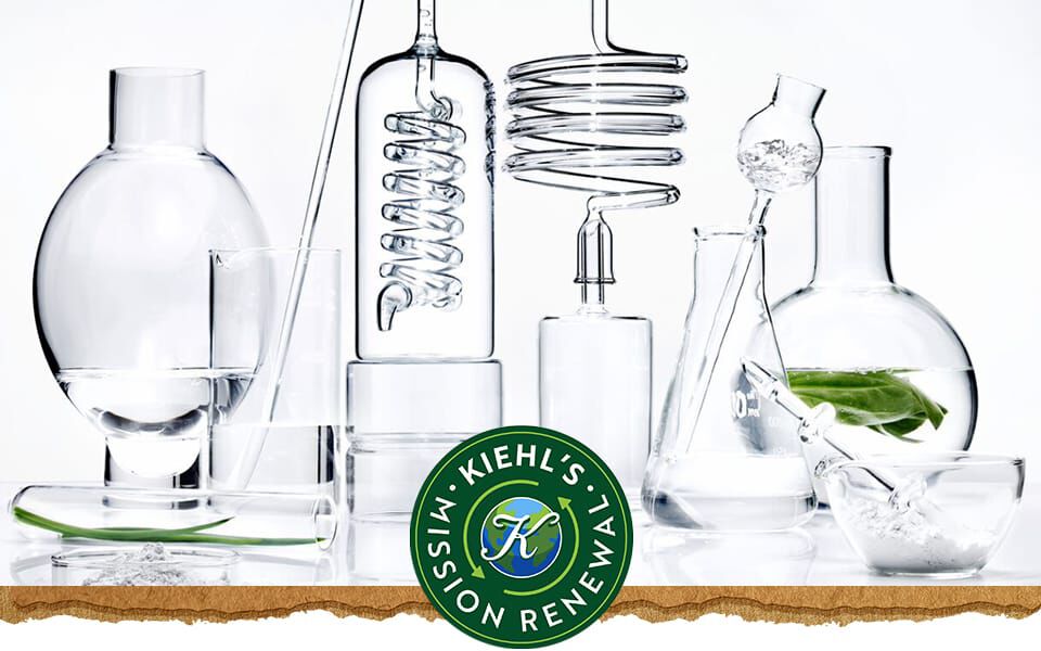 En samling laboratoriekarl i klarglas fyllda med vatten och ett gront lov med Kiehl's logotyp till hoger.