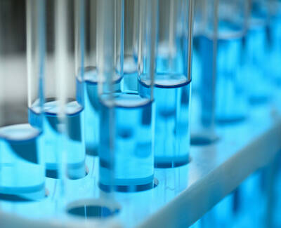 Close-up of test tubes filled with a vivid blue liquid, arranged in a laboratory rack, with a soft blue light illuminating the scene.