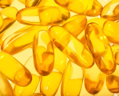 A close-up of transparent yellow gel capsules scattered on a light background.