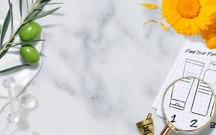 A flat lay featuring a marble background with various natural ingredients like olive branches and flowers, alongside a magnifying glass over a chart with numbered skincare formulas. A mortar and pestle are also visible, suggesting a focus on herbal remedies or skincare preparation.