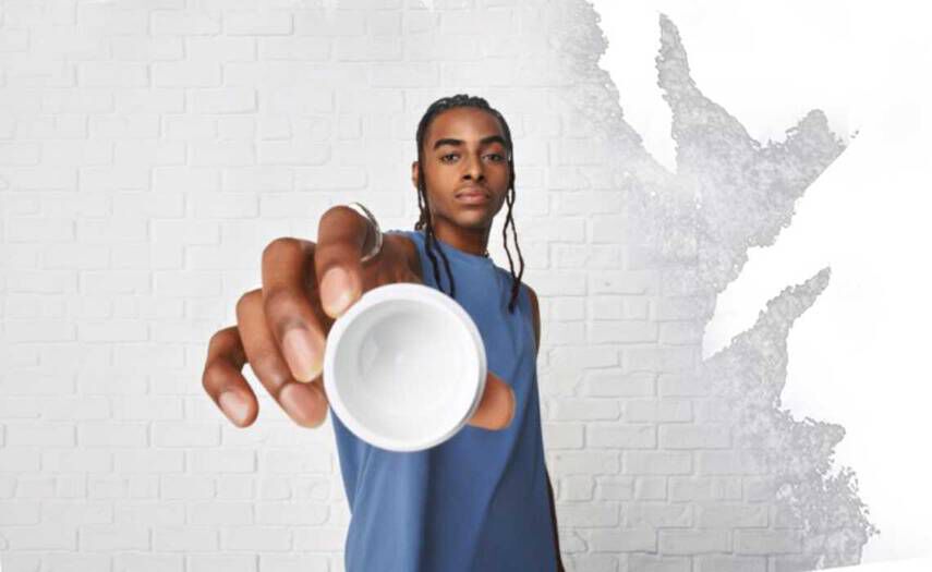 En person i blå armlos skjorta håller en liten vit skål mot kameran, som står mot en vit vagg med textur.