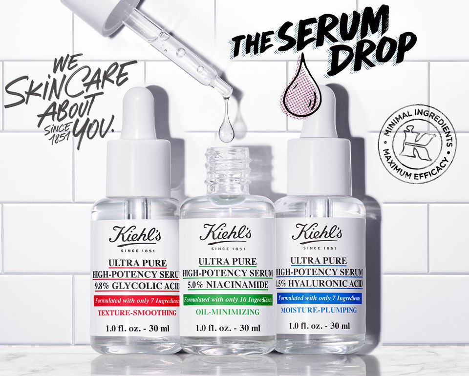 Tre flaskor med serum från Kiehl's på en vit kaklad bakgrund, med texten "THE SERUM DROP" och en droppsymbol.