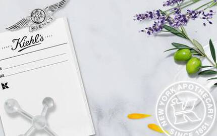 Alt-text på svenska: "Kiehl's historiska foto från deras apotek i New York, omgiven av lavendel, oliver och blomblad, med deras logotyp och text som visar grundandet 1851."