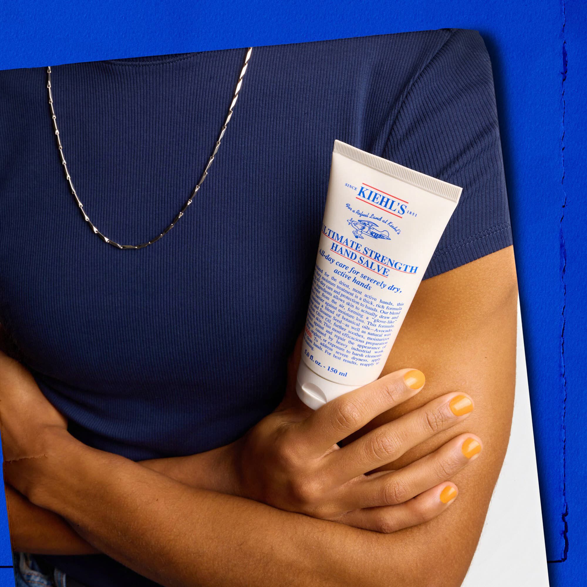 Modell som håller en tub Kiehl's Ultimate Strength Hand Salve