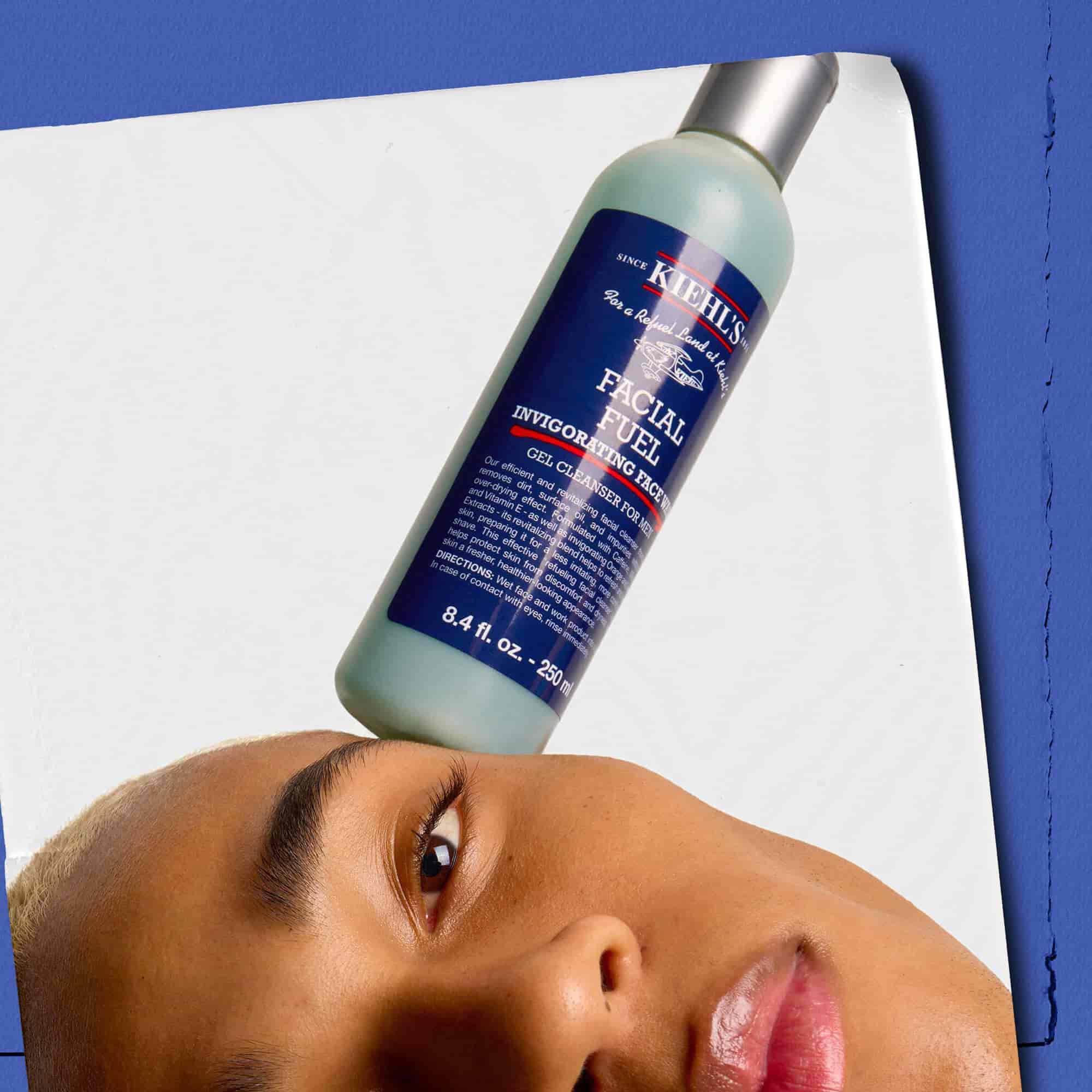 Modell med en flaska Kiehl's Facial Fuel Energizing Face Wash balanserad på ansiktet